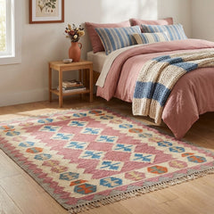 Bedroom with a colorful patterned kilim rug, bed with pink bedding, and side table with books and flowers.
