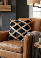 Black and tan cowhide patchwork cushion with lattice design styled on a tan leather armchair