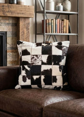 Black and white checkered cowhide patchwork cushion styled on a brown leather sofa