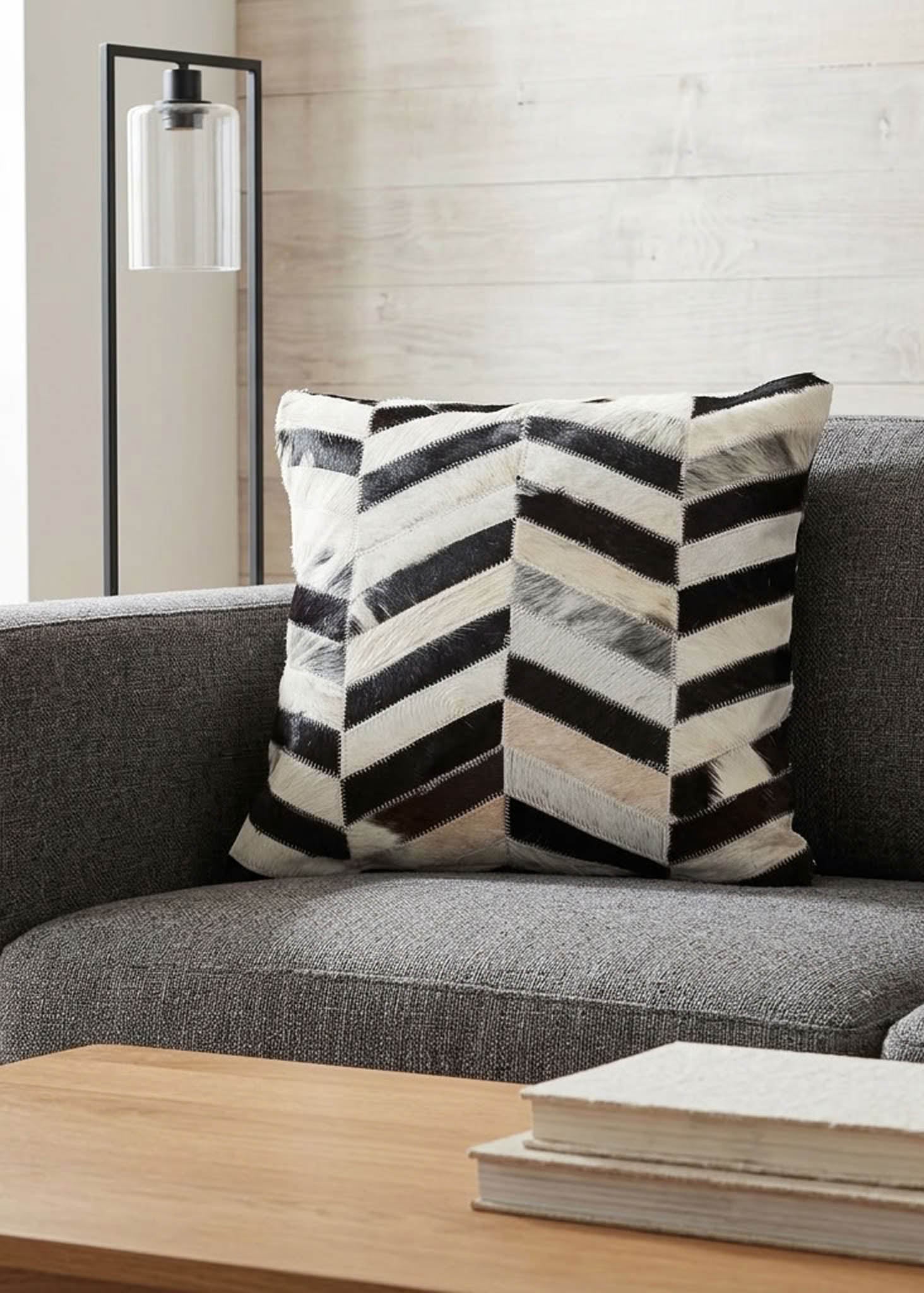 Black and white chevron cowhide patchwork cushion styled on a grey sofa in a modern living room