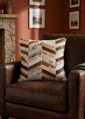 Brown and ivory chevron cowhide patchwork cushion styled on a dark brown leather armchair