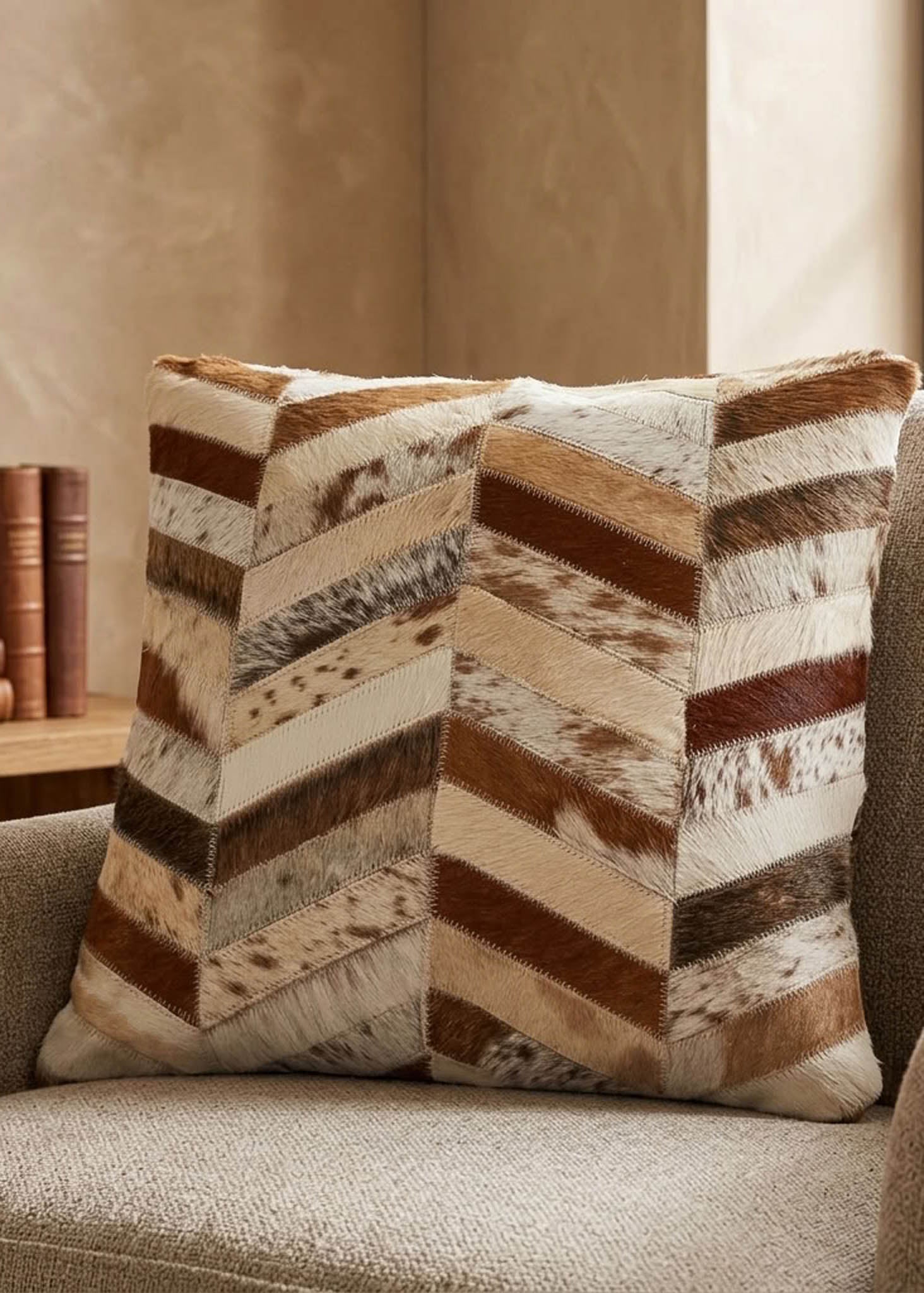 Brown and ivory chevron cowhide cushion styled on a neutral armchair in a warm contemporary interior