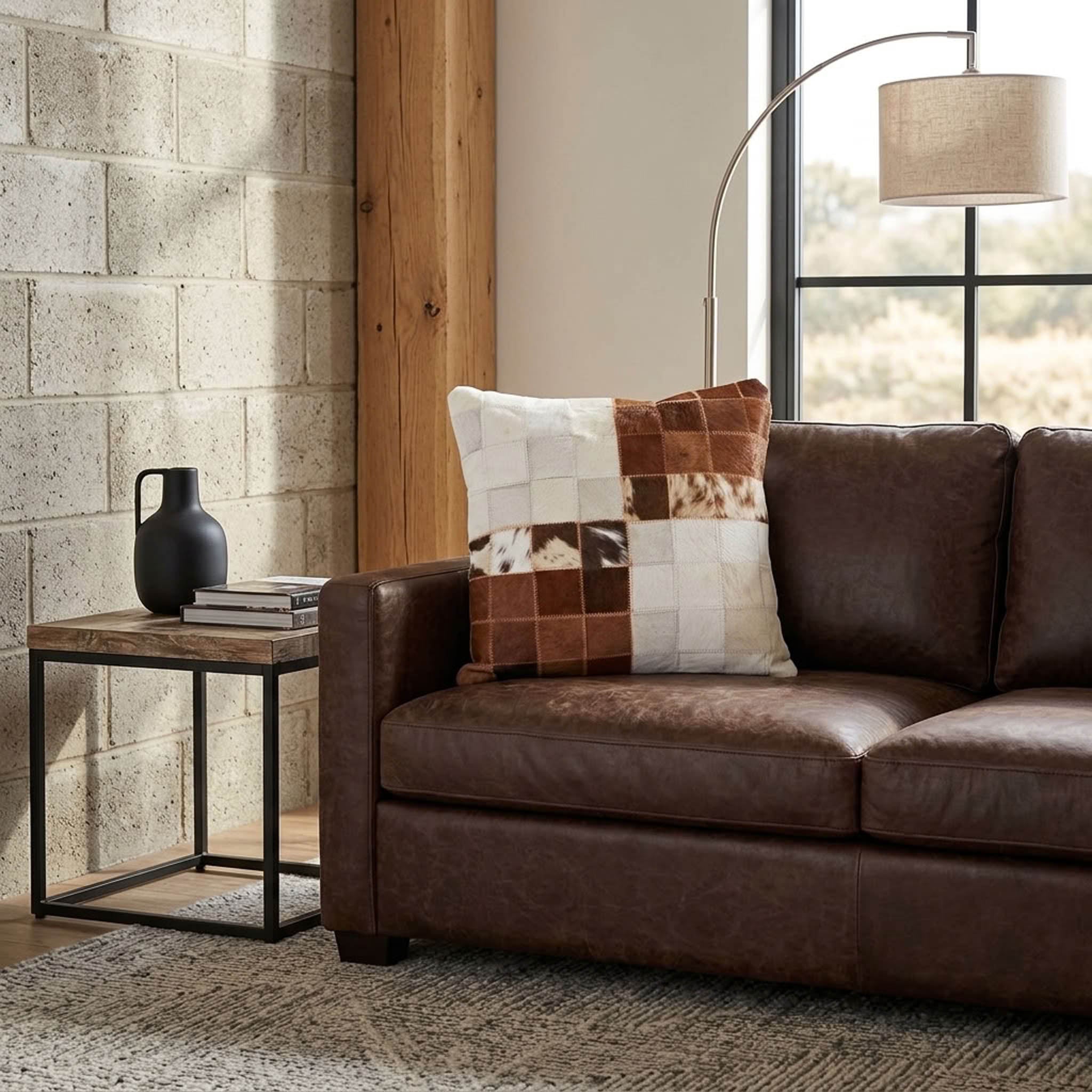 Brown and white color block cowhide patchwork cushion styled on a dark brown leather sofa