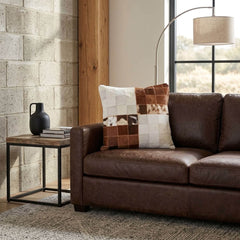 Brown and white color block cowhide patchwork cushion styled on a dark brown leather sofa