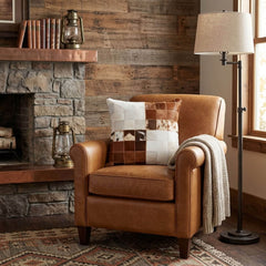 Brown and white cowhide patchwork cushion on a tan leather armchair in a rustic living room