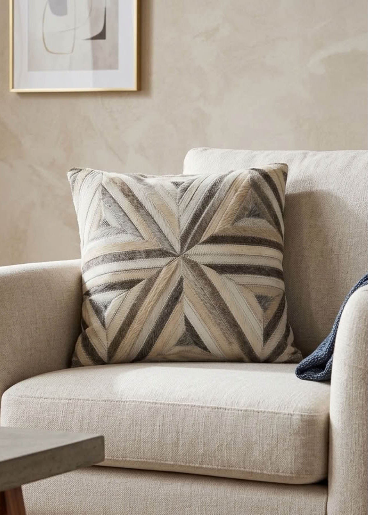 Ivory and grey radiant cowhide cushion styled on a cream armchair in a neutral contemporary interior
