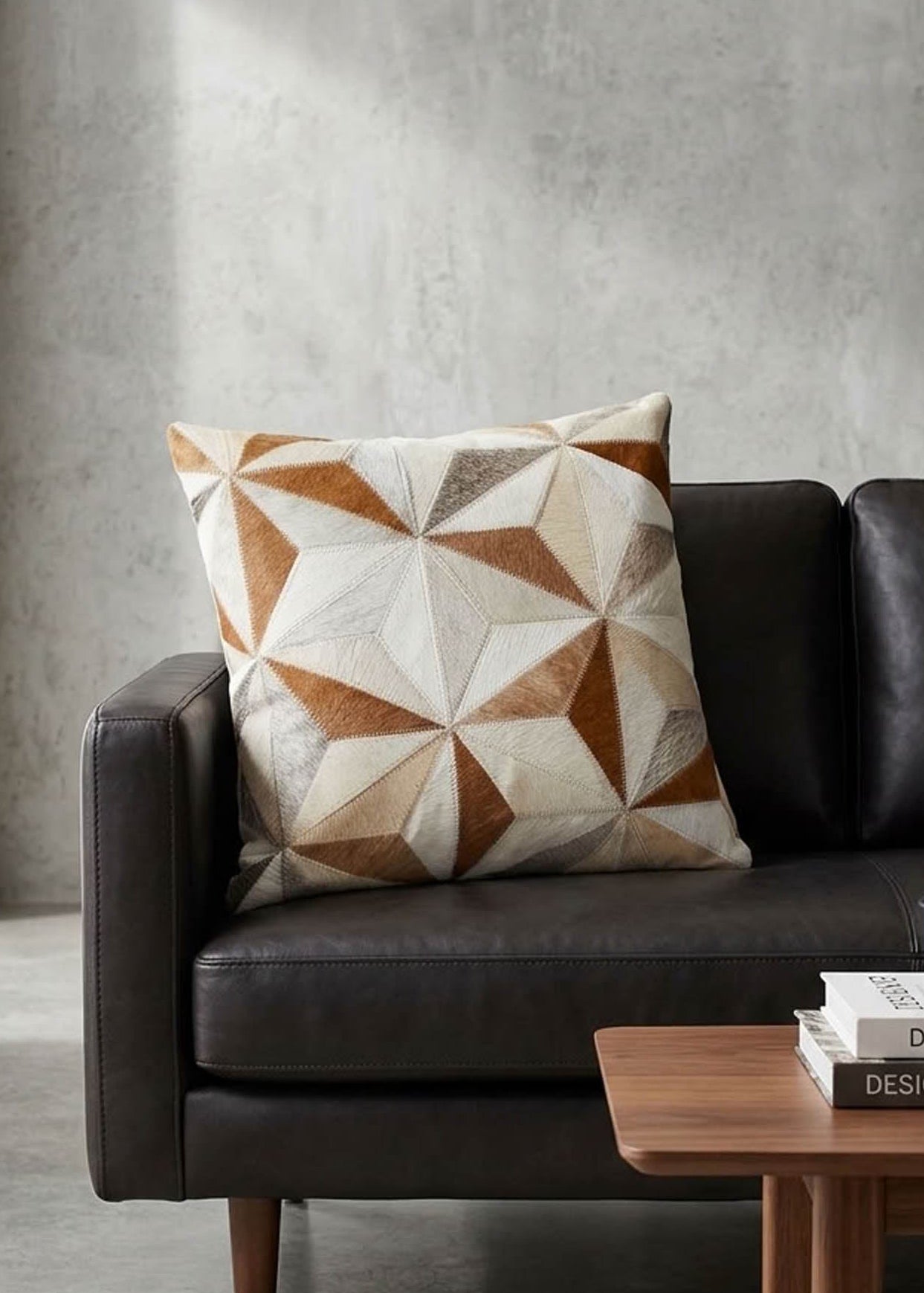 Tan and ivory faceted cowhide patchwork cushion styled on a black leather sofa