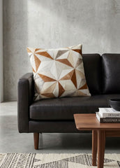 Tan and ivory faceted cowhide patchwork cushion styled on a black leather sofa
