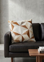 Tan and ivory faceted cowhide patchwork cushion styled on a black leather sofa