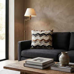 Tricolor chevron cowhide cushion styled on a charcoal sofa in a warm contemporary interior