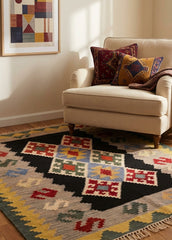 Beige armchair with patterned cushions on a colorful geometric kilim rug in a room with a framed abstract painting.