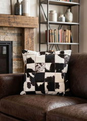 Black and white checkered cowhide patchwork cushion styled on a brown leather sofa
