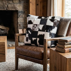 Black and white cowhide patchwork cushion on a rustic leather armchair
