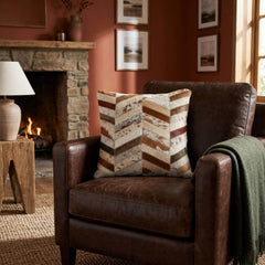Brown and ivory chevron cowhide patchwork cushion styled on a dark brown leather armchair