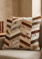 Brown and ivory chevron cowhide cushion styled on a neutral armchair in a warm contemporary interior