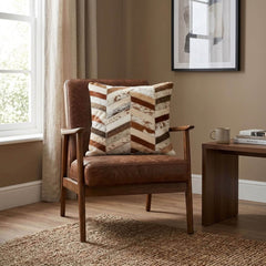 Brown and ivory cowhide patchwork cushion with chevron design styled on a tan leather armchair