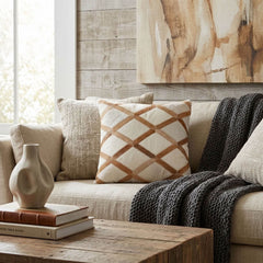 Tan and ivory lattice cowhide patchwork cushion styled on a cream sofa in a warm neutral living room
