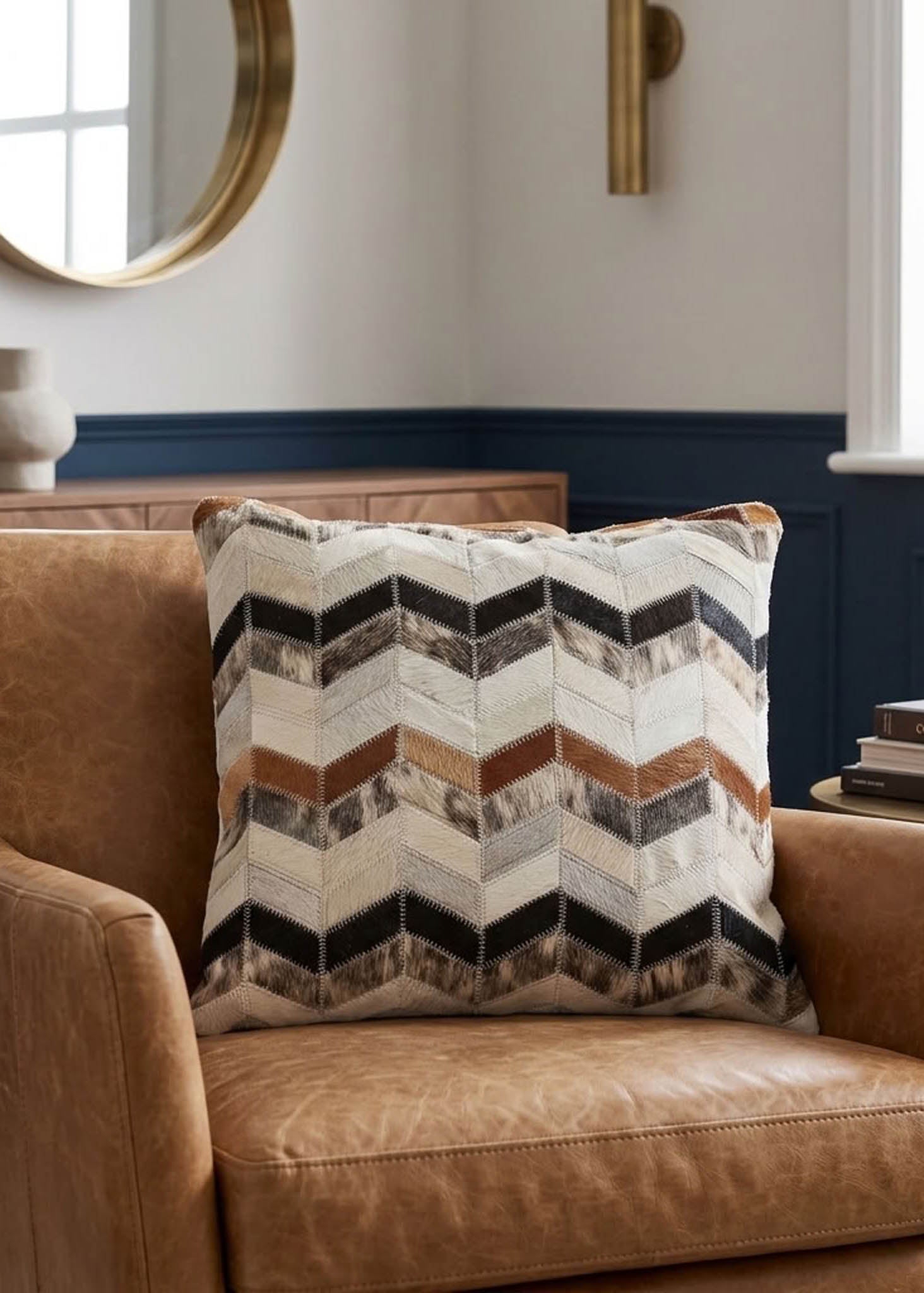 Tricolor chevron cowhide patchwork cushion styled on a tan leather armchair